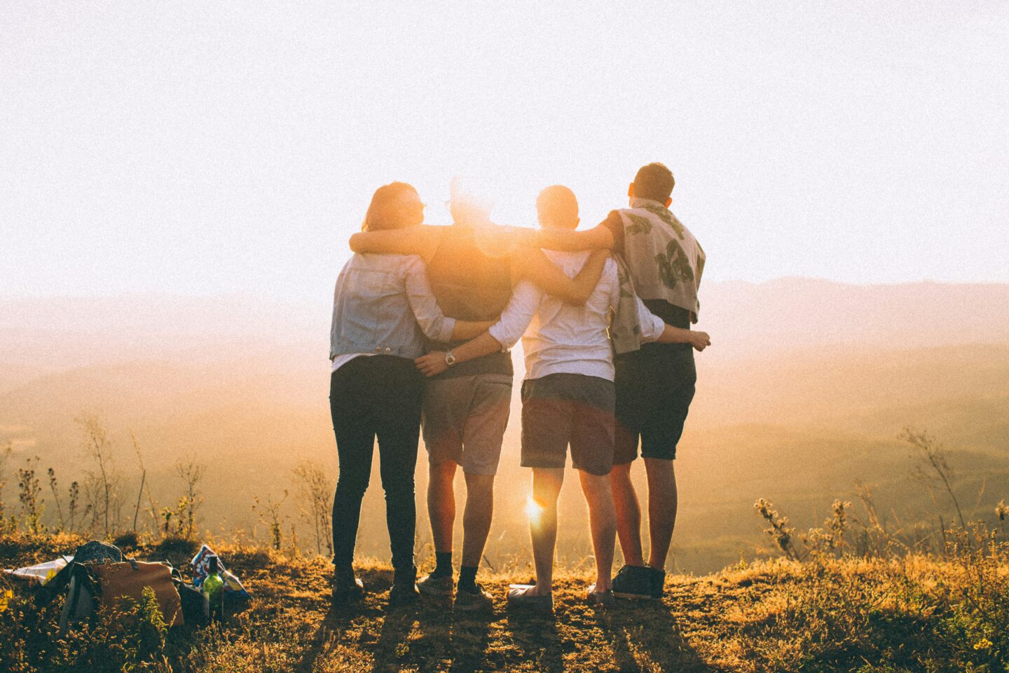 four people stand on mountain facing the sunset