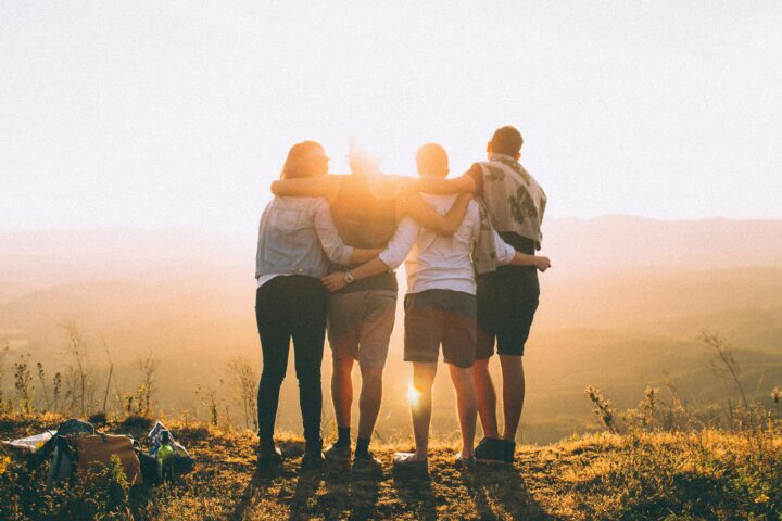 four people stand on mountain facing the sunset